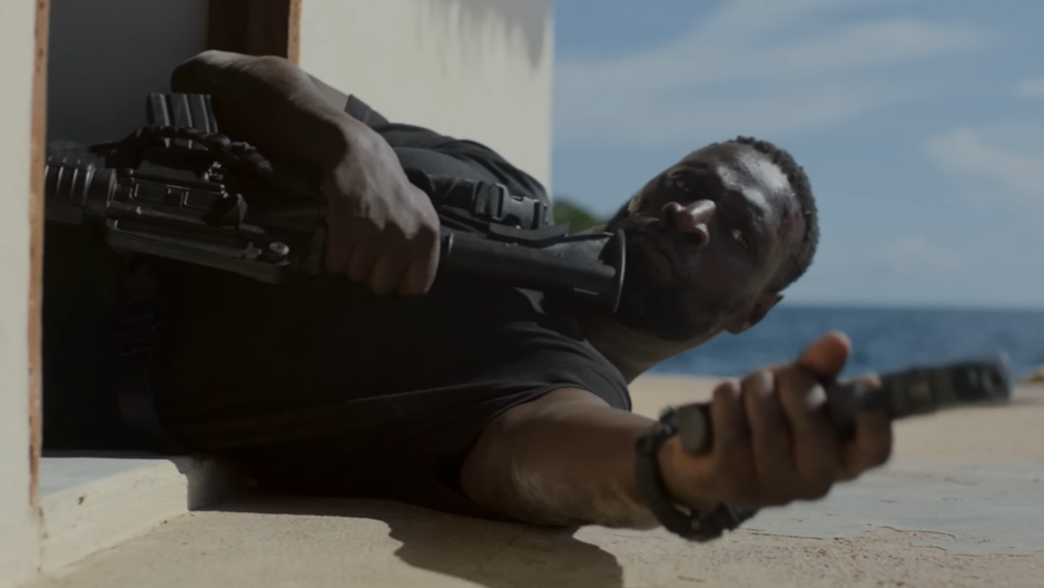 Omar Sy crawling out of a door space aiming a gun towards his target