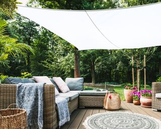 A white shade sail over an outdoor seating area with corner sofa and rug