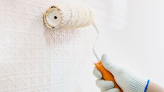 a person painting over wallpaper with a roller