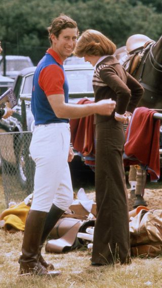 Prince Charles, Prince of Wales, wearing jodhpurs and riding boots, smiles as he stands next to his girlfriend and sister of Lady Diana Spencer, Lady Sarah Spencer (later Lady Sarah McCorquodale) at Guards Polo Club in June 1977 in Windsor, United Kingdom.
