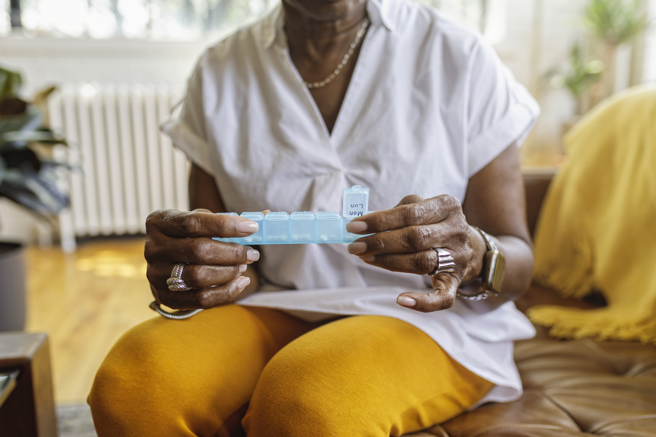 Older black woman sitting on a couch holding a pill box.