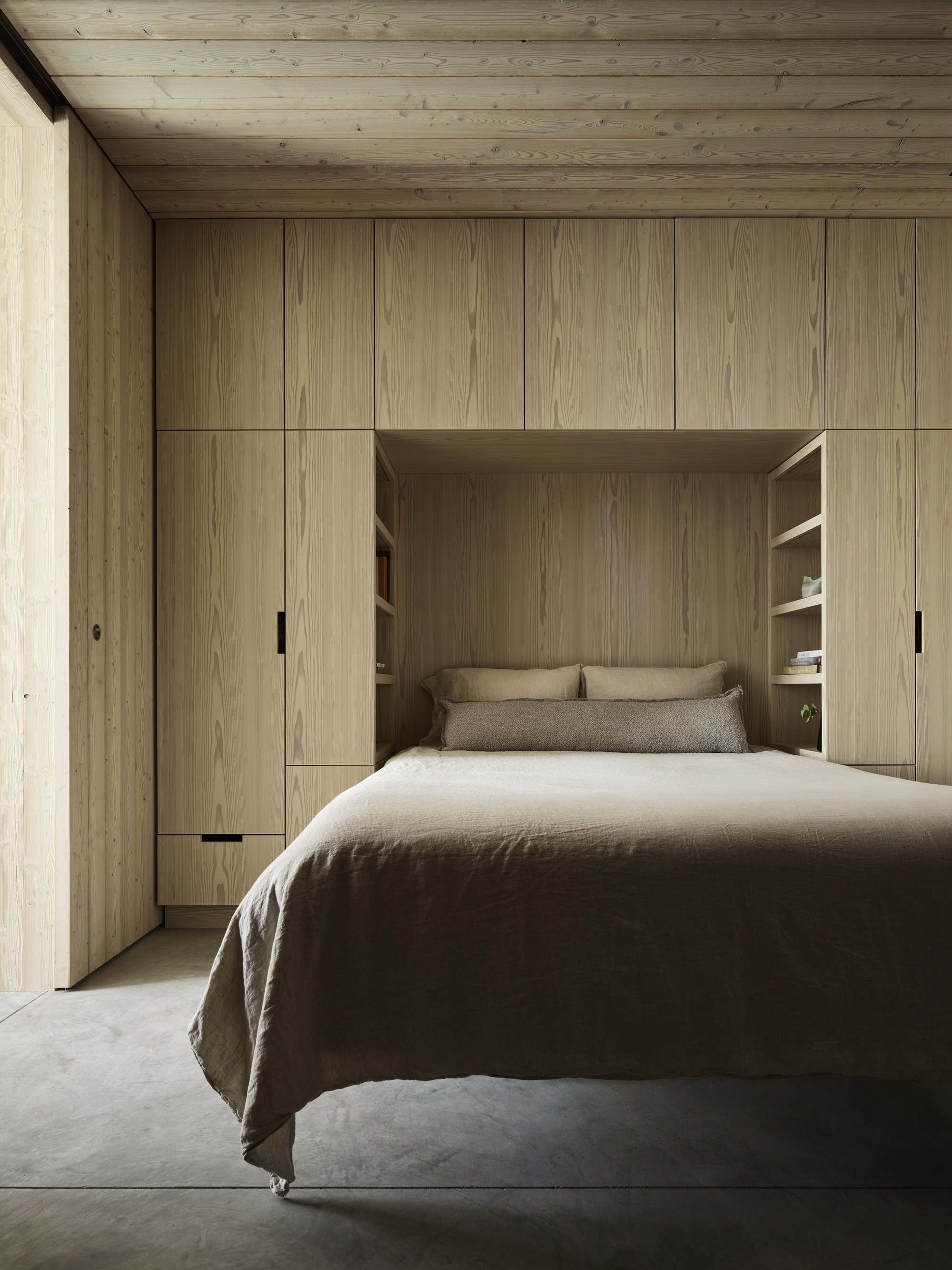 modern bedroom with timber cabinets built around bed, timber panel ceiling, polished concrete floors