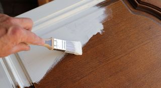 Person painting a kitchen cupboard white with a brush