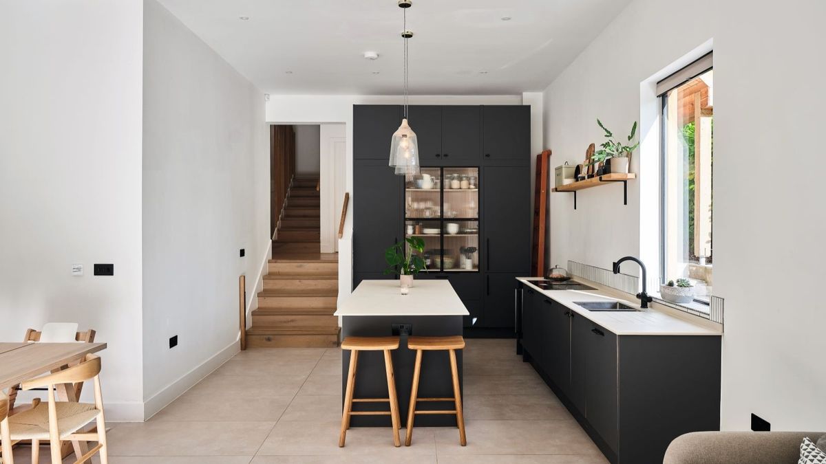 A dark indigo kitchen with white worktops and wooden stools and stairwell