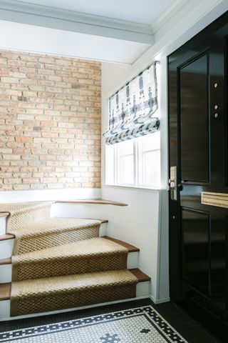 Entryway with neutral stairs above a bare brick wall and open door.