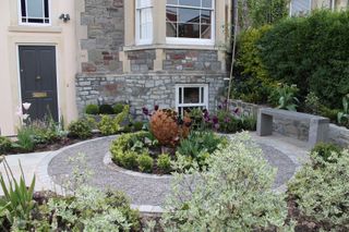 small front garden ideas: modern front plot with sculpture and round flowerbed