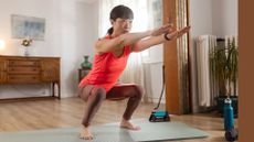 Woman doing deep squat with resistance band on yoga mat in living room, arms outstretched