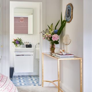 corner of bedroom with gold console table and flowers leading into en suite bathroom