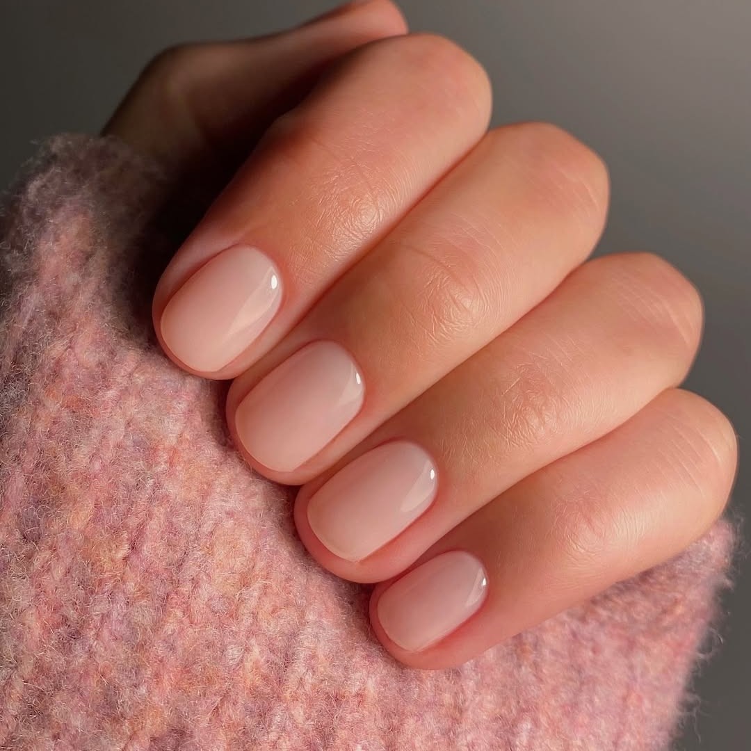 A set of light pink-painted nails held against the sleeve of a pink sweater.
