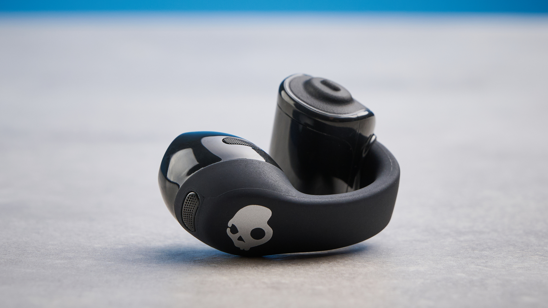 Skullcandy Push 720 Open in black and silver colorway with charging case photographed on a blue background