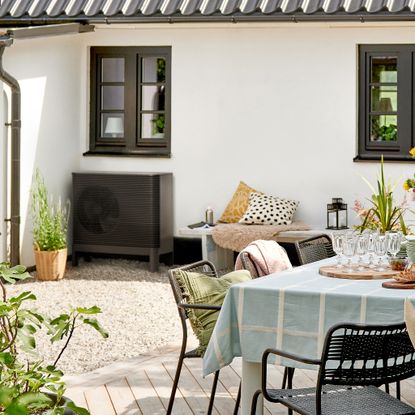 An IKEA x Aira air-to-water heat pump installed on a house with a dressed outdoor dining table next to it