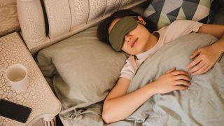 Woman wearing sleep mask in bed with phone turned off beside the bed, to represent good sleep hygiene