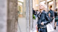 An older, attractive woman is windown shopping in Italy. She looks chic in a leather jacket.