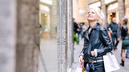 An older, attractive woman is windown shopping in Italy. She looks chic in a leather jacket.