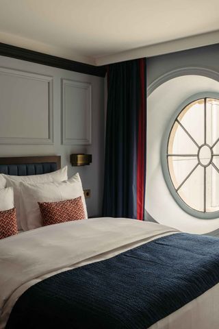 Ameron bedroom with grey wall panelling, navy curtains and bed linen and round porthole window