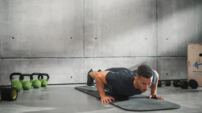 A man performing push ups in the gym with some kettlebells by the side of him