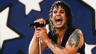 A man with long hair grips a microphone while singing