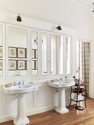 A white bathroom with panelling with mirrors over double basins