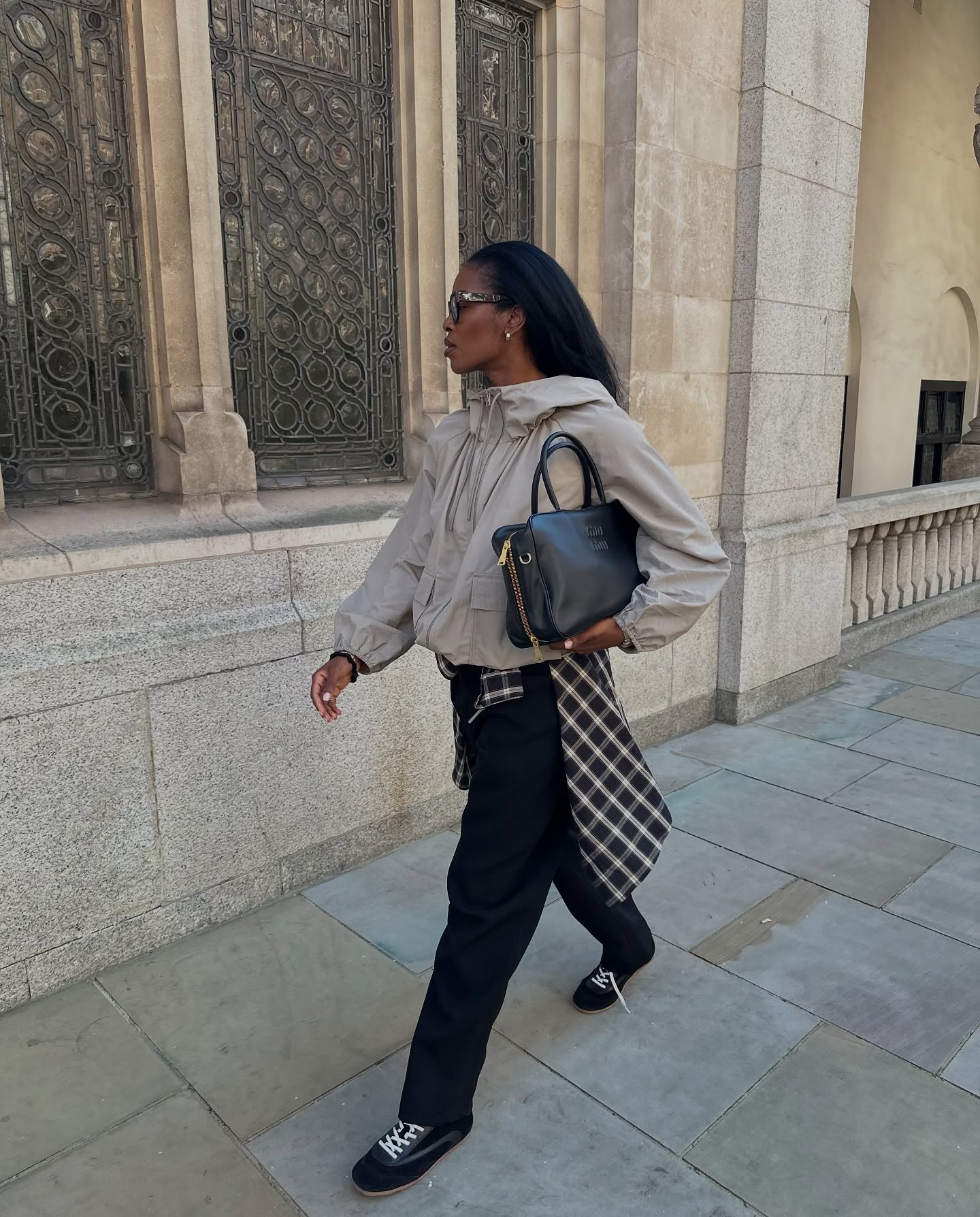 @nlmarilyn wearing a tan jacket, black tailored trousers, black sneakers, and a flannel shirt tied around her waist.