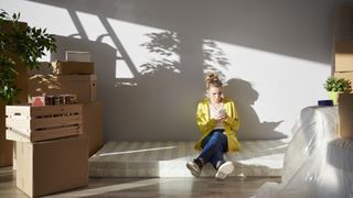 A woman sits on a mattress placed on the floor after she just moved it