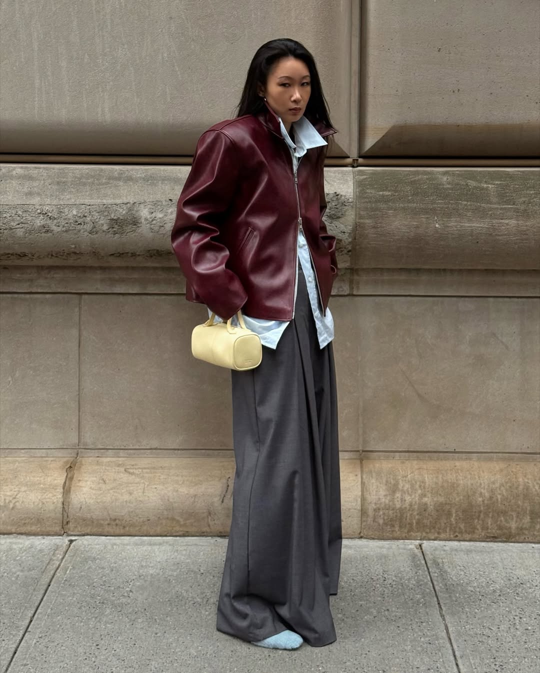A woman wears a light yellow bag with a dark red jacket.