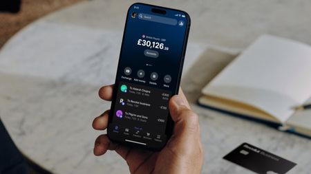 An outstretched hand holds a smartphone displaying the Revolut app