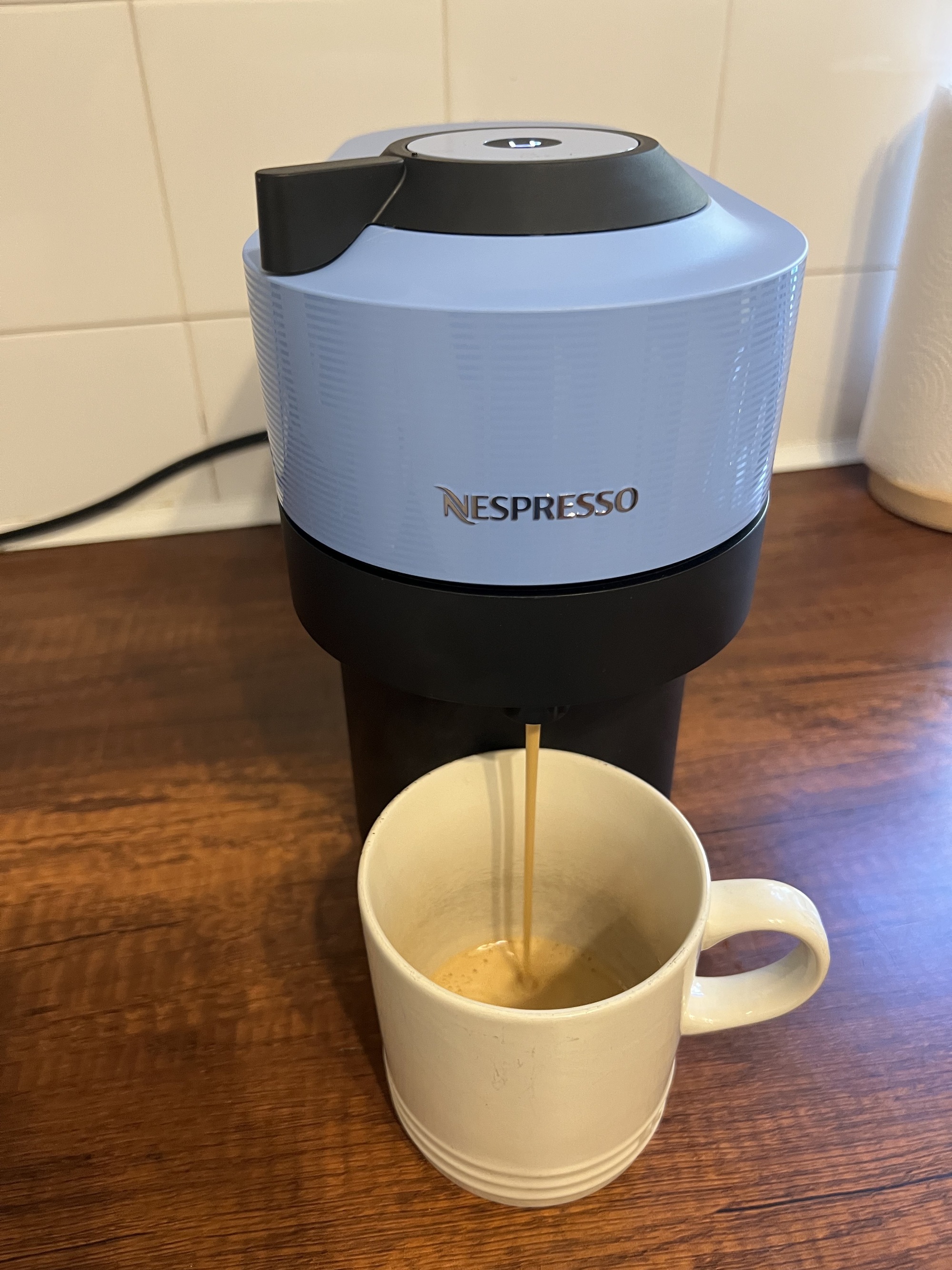 Image of a shot of espresso being brewed into a mug from a light blue and black Nespresso Vertuo Pop pod machine