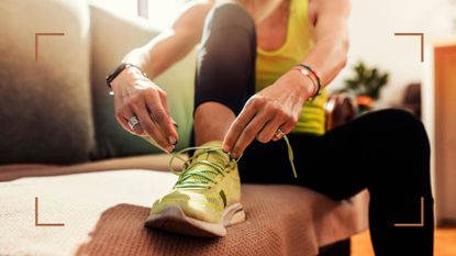 Woman sitting down on couch wearing workout clothes and tying shoelaces up as she tries running 30 minutes a day, sunshine coming through window 