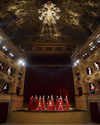 The theatre’s circular auditorium, various balconies. On the stage itself is a collection of dresses in Valentino red from across the archive.