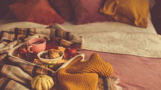 A bed decorated in fall colors like oranges and yellows, with pillows, blankets, and a tray of pumpkins on top