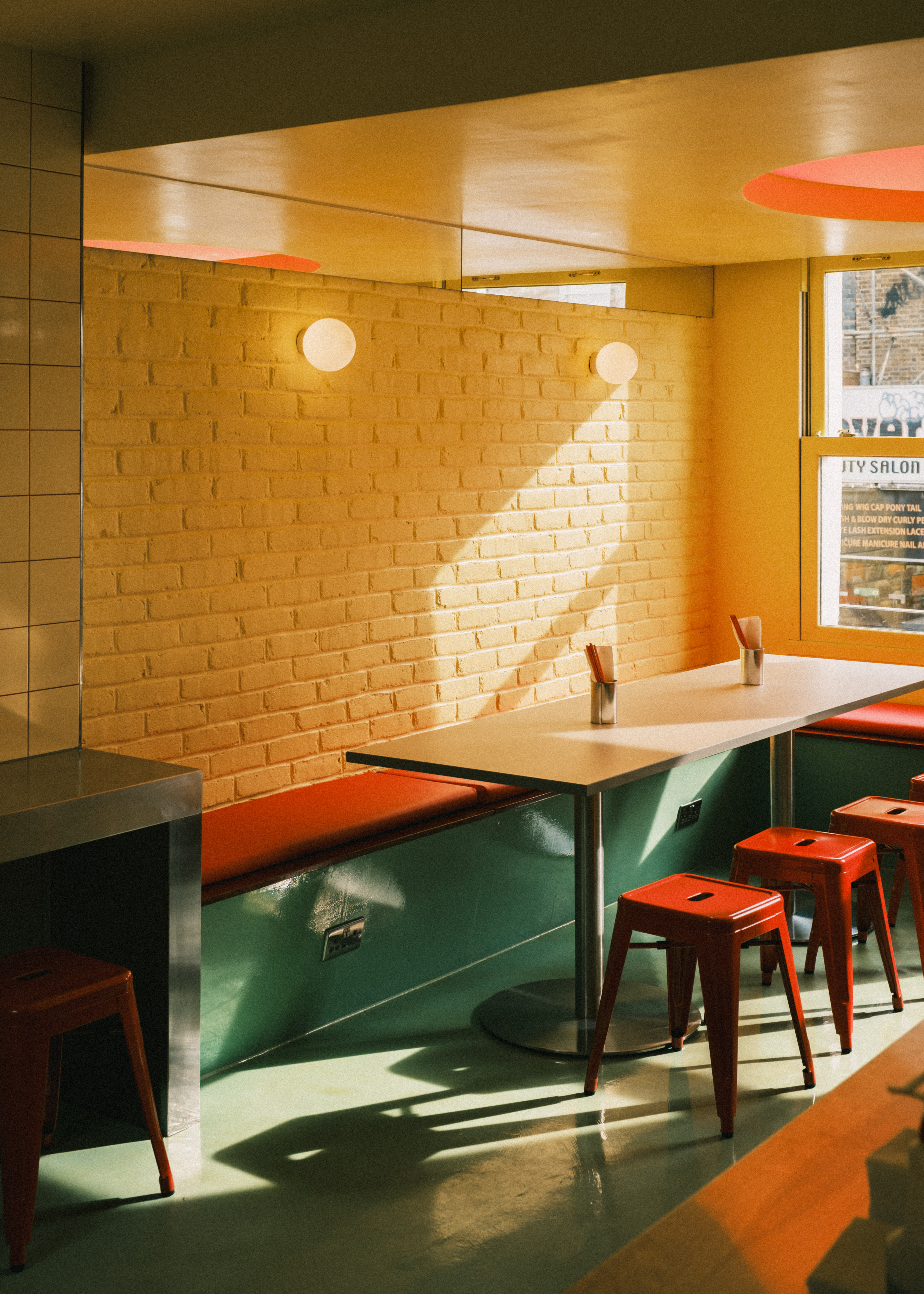 An inventively designed, small eatery boasts buttery brick walls, sleek green floors, red banquettes and metal chairs, and spherical, softly glowing opaque glass sconces.