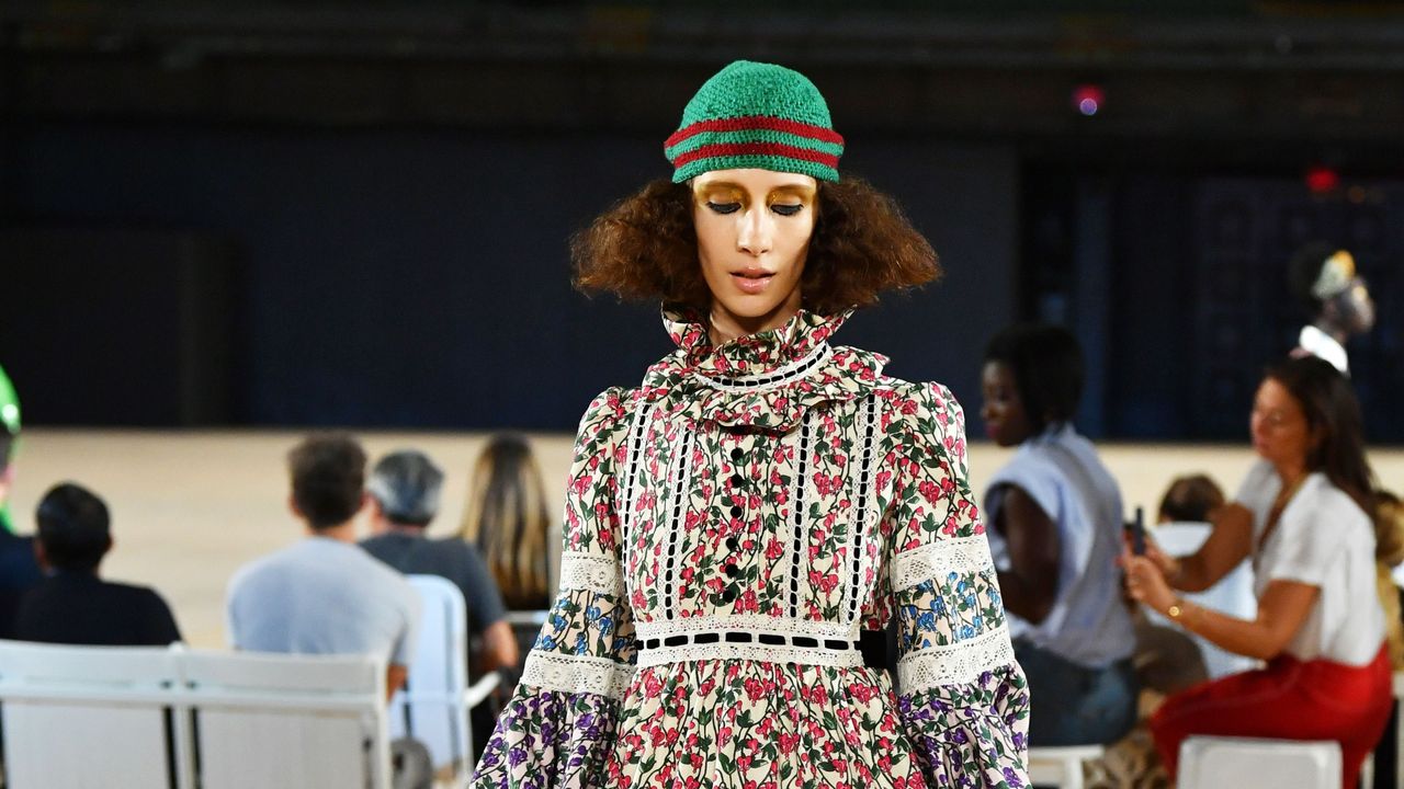 A woman wearing a green beanie hat and long floral dress on the cat walk