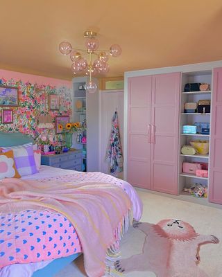 A pink bedroom with floral wallpaper, a pink bed, and a pink wardrobe
