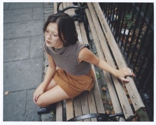 Actress Lukita Maxwell, sitting on a bench in a public park.