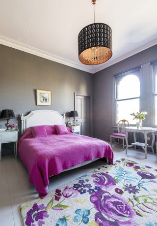 Bedroom featuring striking pink bed, white headboard, floral rug and decorative copper-effect lampshade