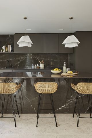 An example of designing a kitchen island in a dark gray kitchen scheme, with wicker breakfast bar stools and gray marble backsplash.