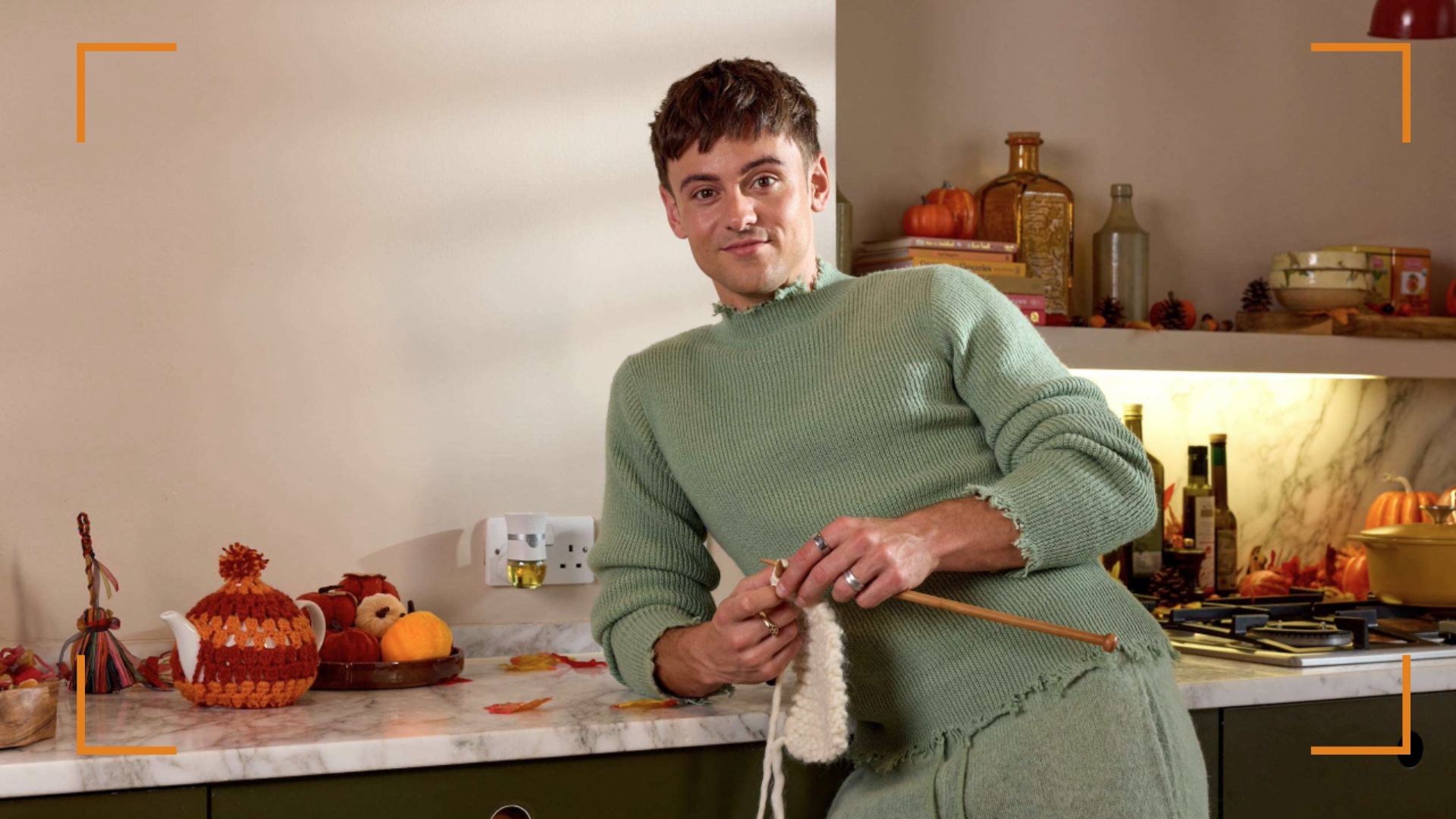 Tom Daley x Air Wick campaign focus with Tom Daley leaning on a counter with knitting
