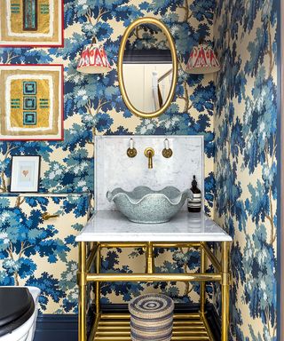 Bold blue floral wallpaper in bathroom with red wall lights and scalloped shape basin