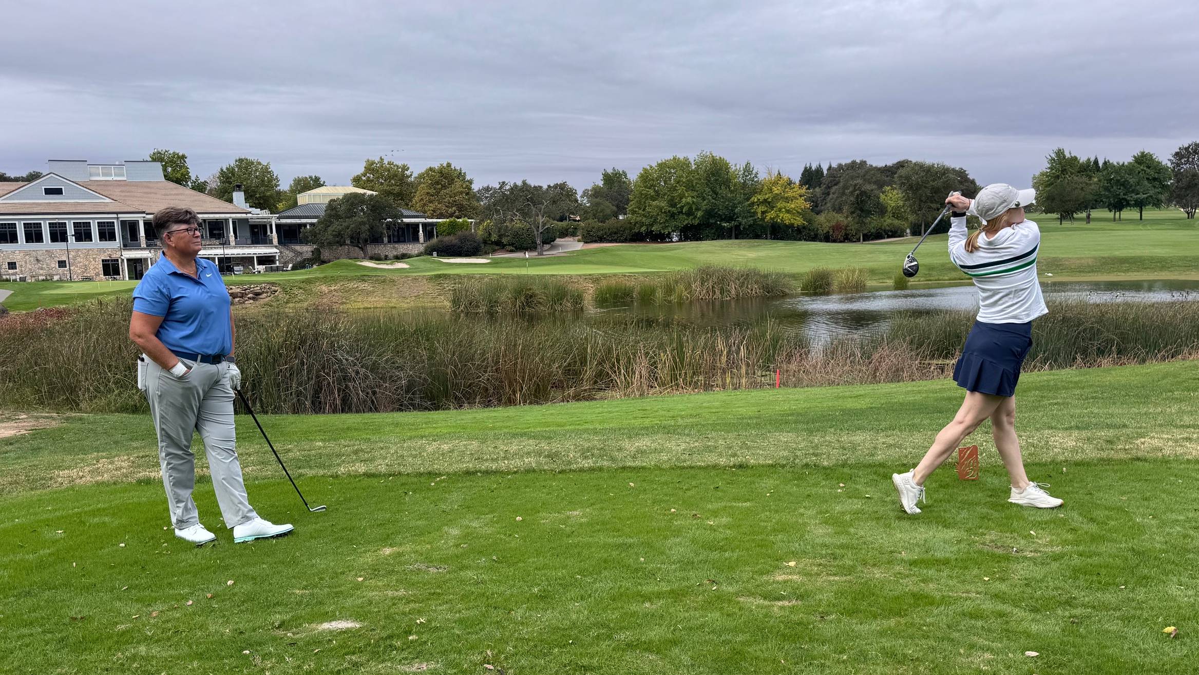 Lauren Katims hitting a hybrid off the tee under the eye of a coach