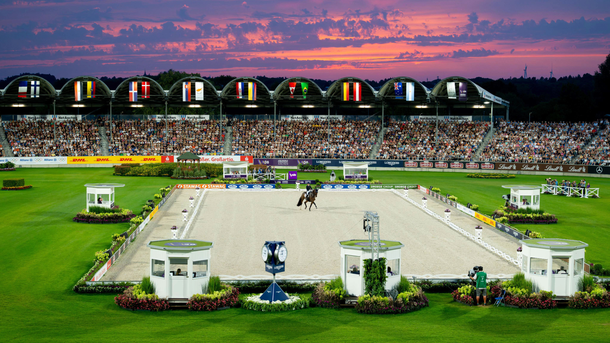 A zoomed out shot of Becky Moody riding Jagerbomb during the freestyle at the 2026 World Dressage Championships in Aachen under a dramatic setting sun