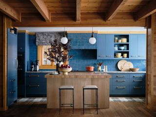 A mainly blue kitchen with wooden island and symmetrical seating and lighting