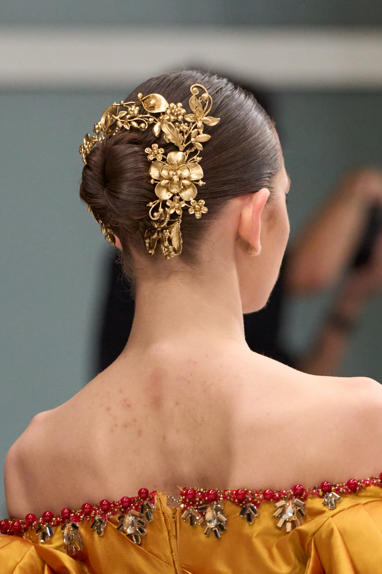 model with dark brunette hair styled in a slicked back bun with gold floral hair accessories secured around the bun