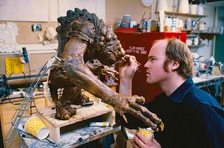 a man paints the face of a small monster puppet