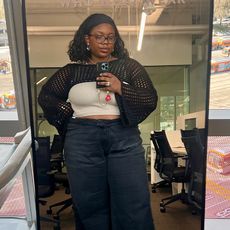 chichi wears crochet bolero, off-white tank, and black jeans while taking a mirror selfie in the office