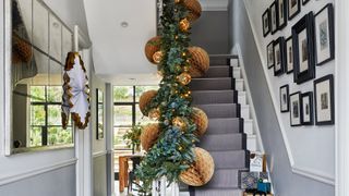 Hallway with striped stair runner and festive garland and oversized paper decorations on the banister to create a Christmas decorating idea