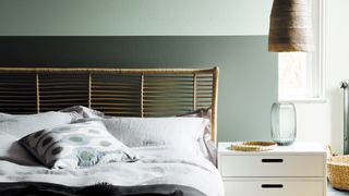 Green bedroom with two-tone bedroom paint colors on the wall behind a rattan bed