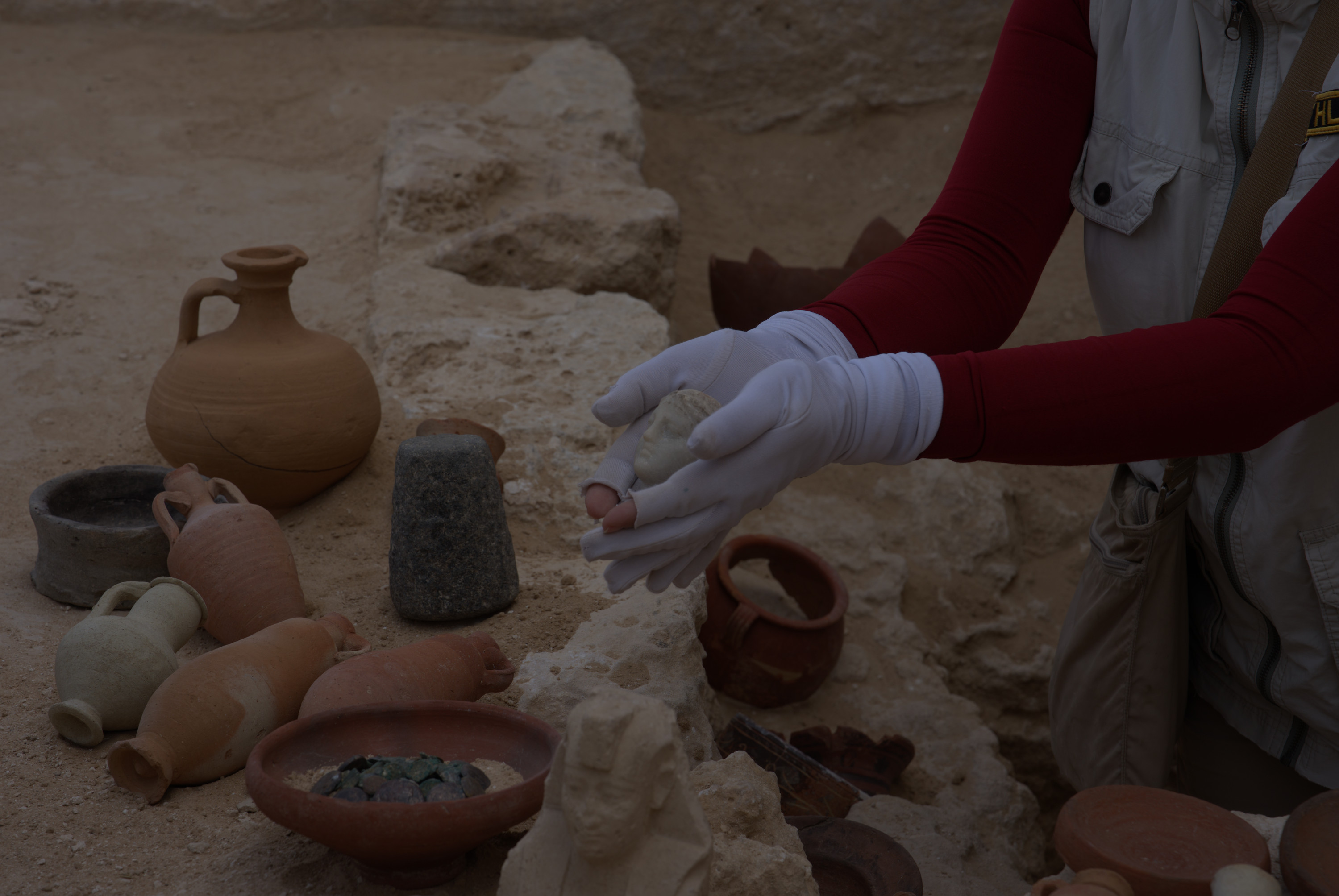 A woman holds a small marble bust in her hands near other artifacts &amp;mdash; ceramic bowls and coins.