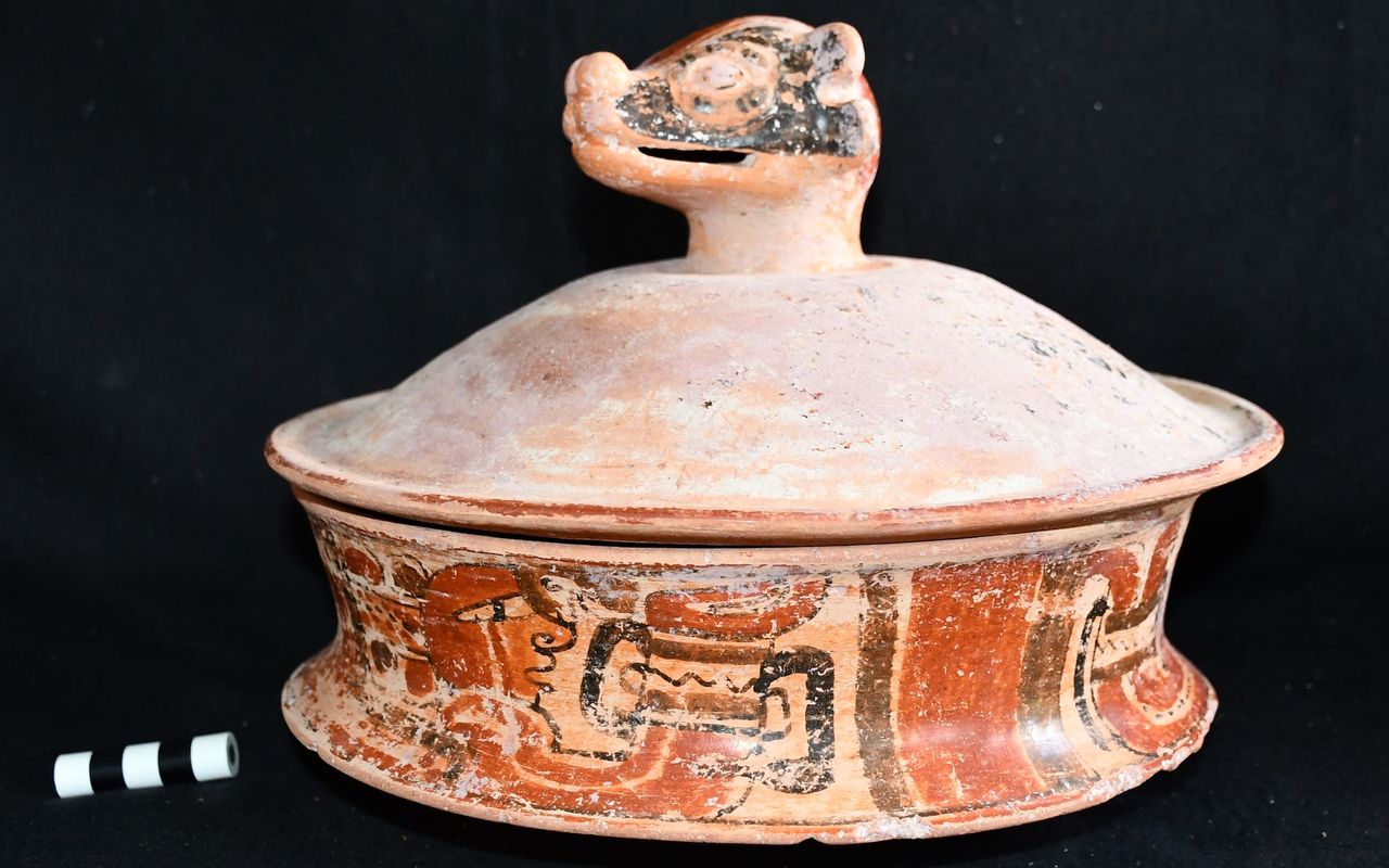 a pottery vessel with painted ornamentation and a lid with the head of an animal