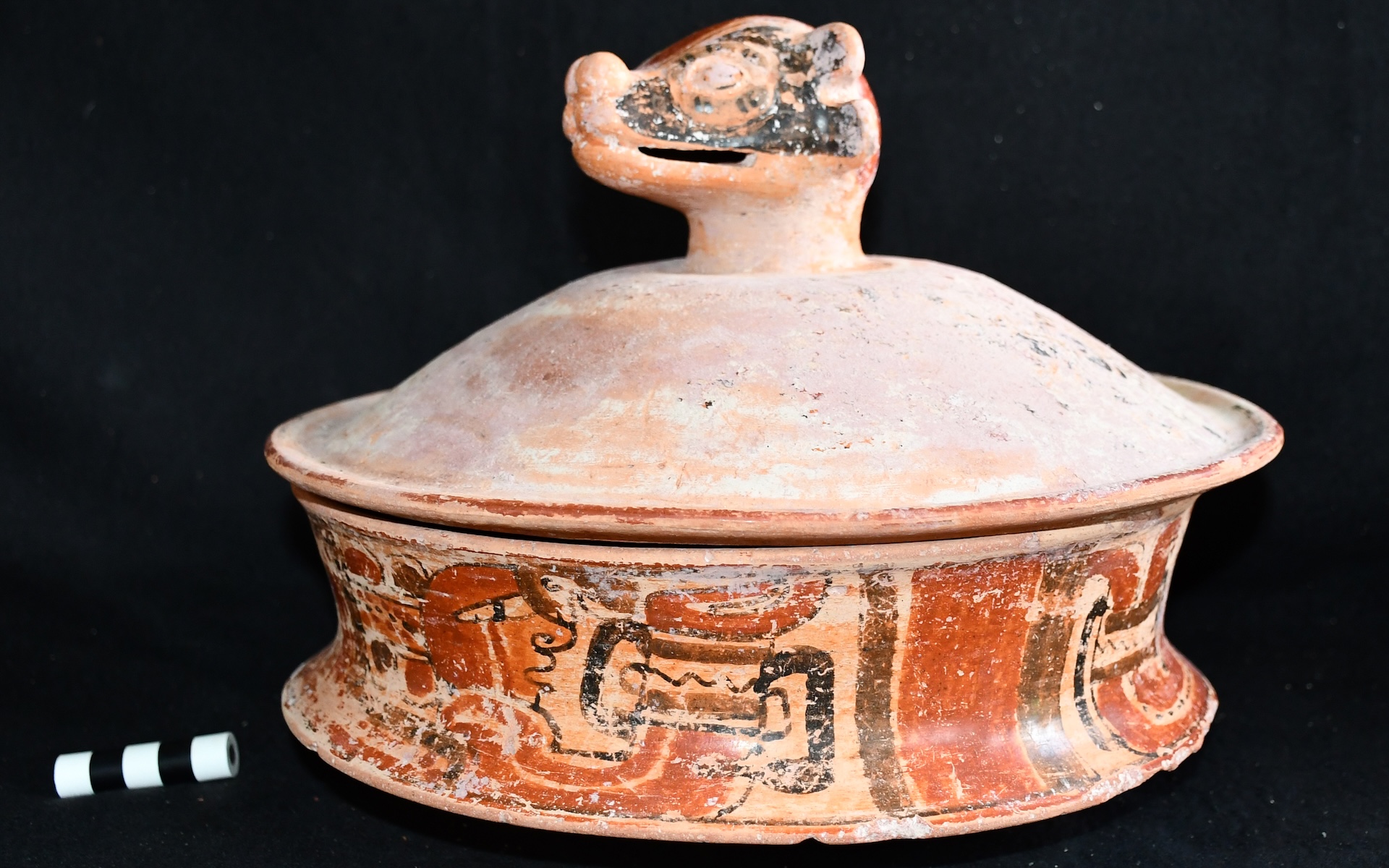 a pottery vessel with painted ornamentation and a lid with the head of an animal 