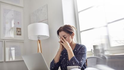 Tired, stressed businesswoman at laptop with head in hands